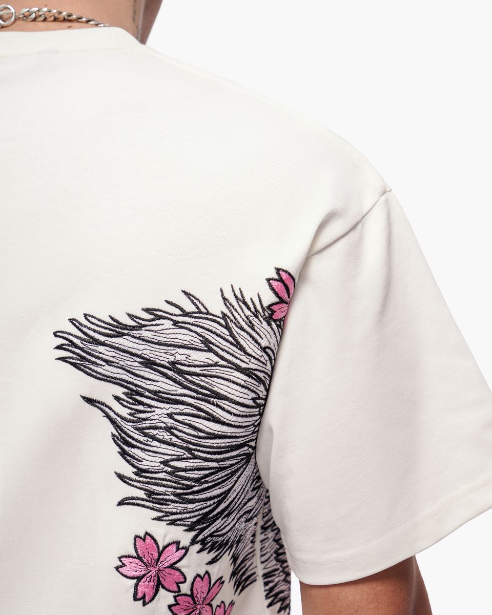White t-shirt with black feather and pink flower design on a white background
