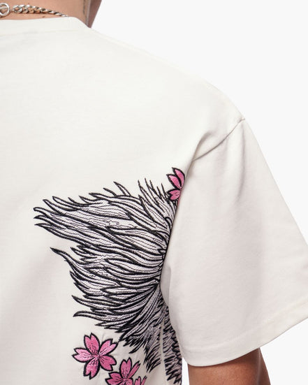 White t-shirt with black feather and pink flower design on a white background