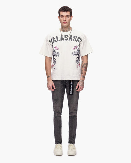 Person wearing a white t-shirt with graphics and text, paired with dark jeans on a white background
