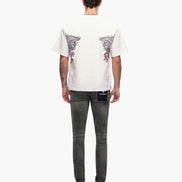 Person wearing a white t-shirt with a graphic design and dark jeans on a white background