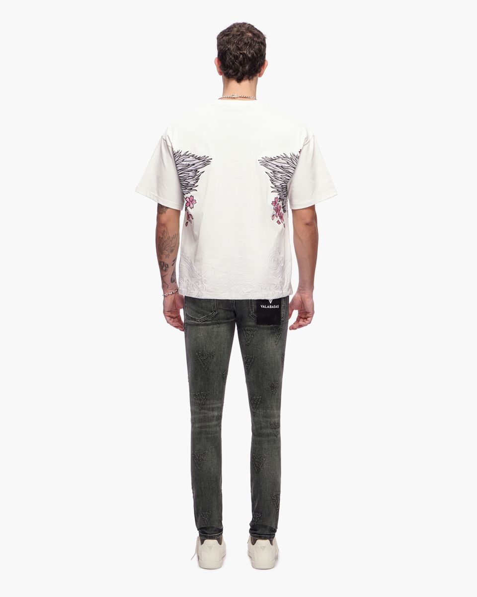 Person wearing a white t-shirt with a graphic design and dark jeans on a white background