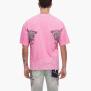 Person wearing a pink t-shirt with black wing designs on the back, standing against a white background.