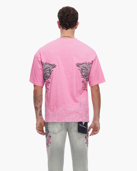 Person wearing a pink t-shirt with black wing designs on the back, standing against a white background.