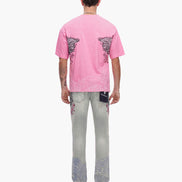 Person wearing a pink t-shirt and light gray jeans with floral designs on a white background