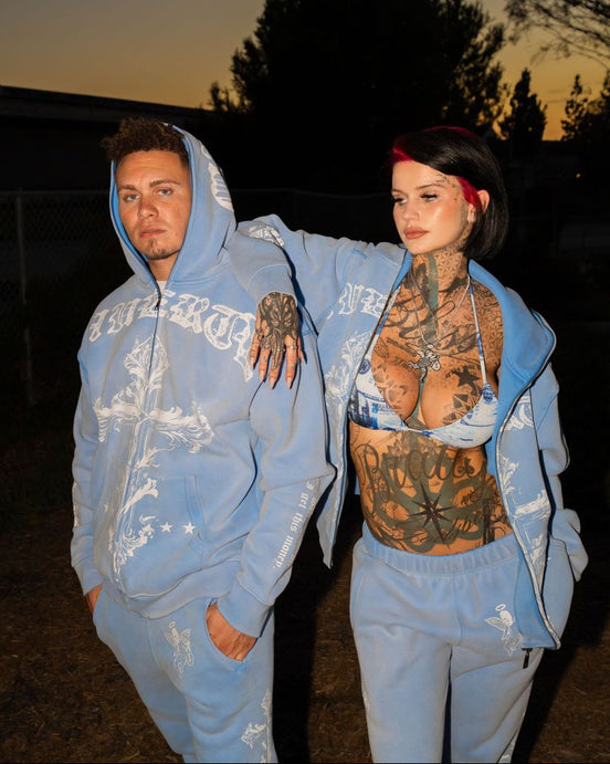 Two people in matching blue outfits standing outdoors at dusk.