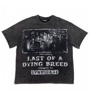 A dark gray washed graphic t-shirt featuring a black-and-white band photo and distressed white text reading 'Presenting Last of a Dying Breed' and 'Designed by Syndicare'.