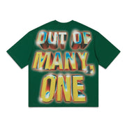 A dark green short-sleeve t-shirt with a large, colorful graphic text print reading 'OUT OF MANY, ONE' in a 3D metallic yellow, blue, and red gradient style, displayed flat against a white background.