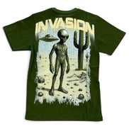 An olive green short-sleeve t-shirt featuring a large graphic print on the front. The graphic depicts a tall alien standing in a desert landscape with a cactus, a UFO, and the word 'INVASION' printed in a distressed cream-colored font above.