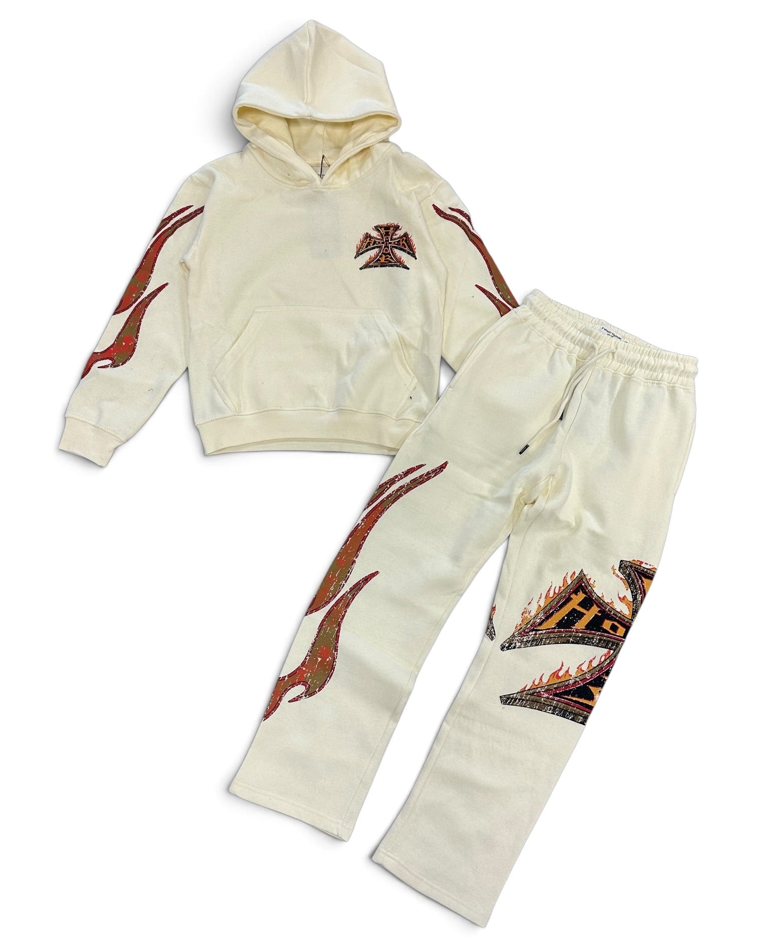 A two-piece kids' loungewear set consisting of a cream-colored cropped hoodie and matching sweatpants, both decorated with red and black flame-like graphics and a small cross emblem on the chest.
