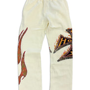 Off-white sweatpants featuring a large red and green flame graphic on the right leg and a black, orange, and yellow tribal-style graphic on the left leg, displayed flat against a white background.