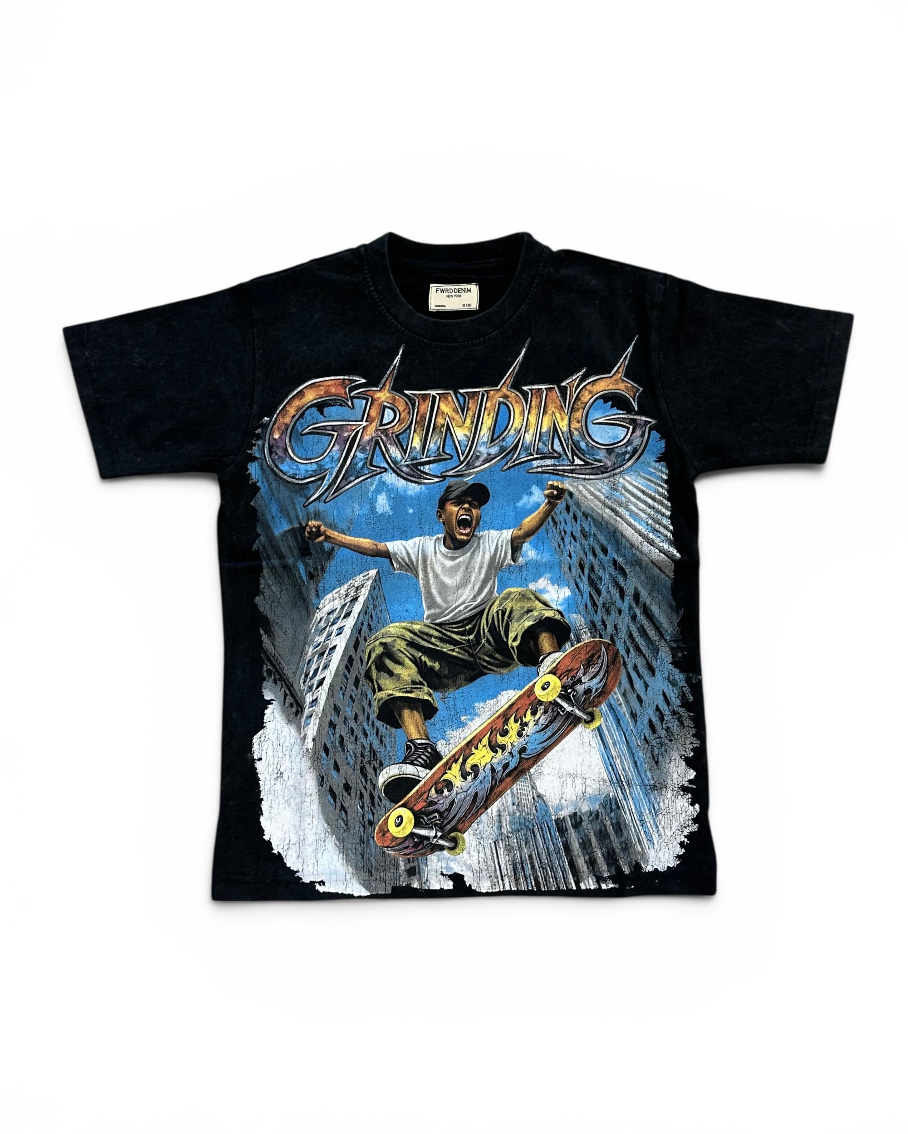A black short-sleeve graphic t-shirt featuring a large front print of a skateboarder in mid-air between tall buildings under the word 'GRINDING' in metallic lettering.