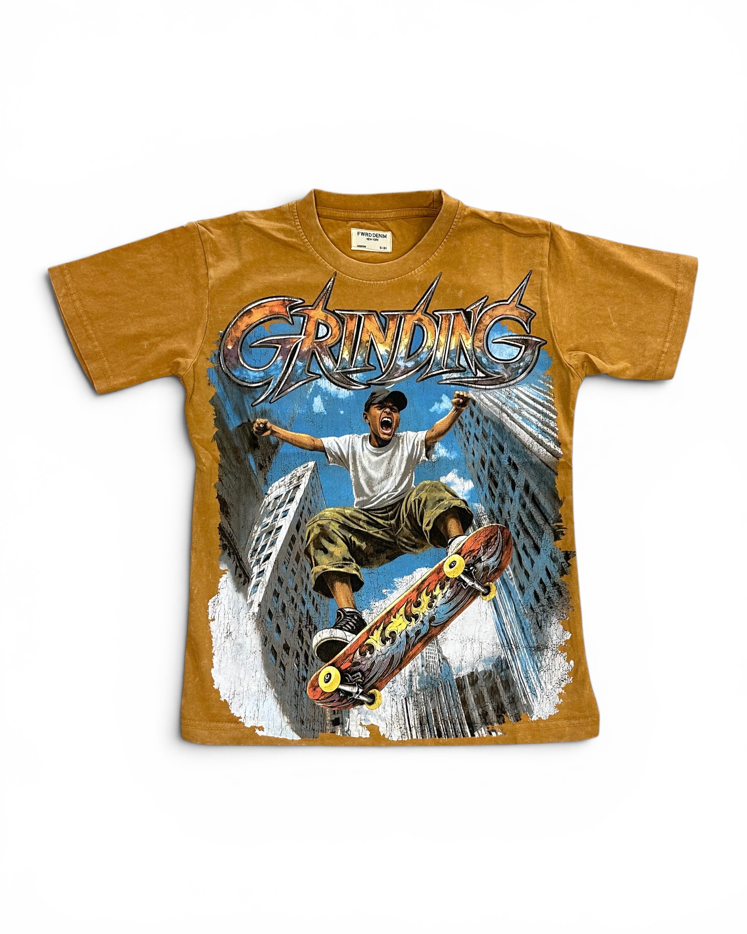 A vintage-style graphic t-shirt in a washed mustard yellow color, featuring a large front print of a skateboarder in a city with the word 'GRINDING' in stylized metallic lettering.