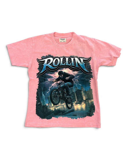 A pink short-sleeve graphic t-shirt featuring a large front print of a mountain biker with the word 'ROLLIN' in stylized blue and white lettering above, set against a plain white background.