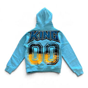 A light blue kids' hooded sweatshirt shown from the back, featuring a large graphic print with the word 'KING' in dark blue letters and the number '00' in yellow, black, and blue.