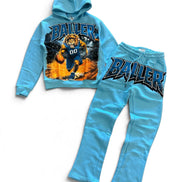 A two-piece kids' sweatshirt and jogger set in light blue, featuring a graphic hoodie with a basketball player and the word 'BALLER' on the front, and matching jogger pants with 'BALLER' printed across the thigh.