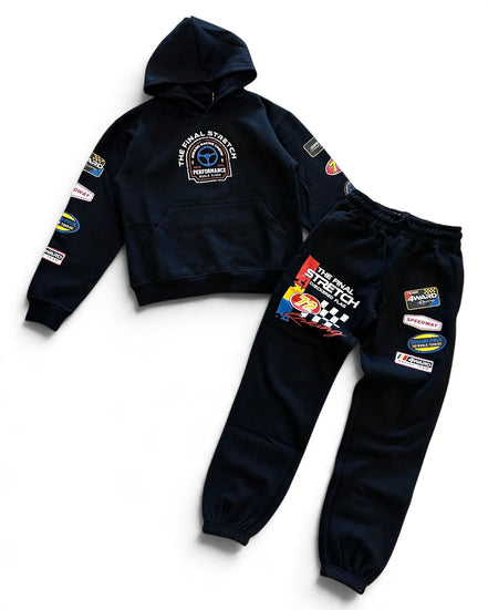 A two-piece kids' racing team hoodie and sweatpants set in dark navy blue. The hoodie features a chest graphic and various sponsor patches on the sleeves.
