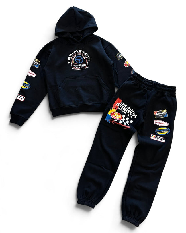 A two-piece kids' racing team hoodie and sweatpants set in dark navy blue. The hoodie features a chest graphic and various sponsor patches on the sleeves.