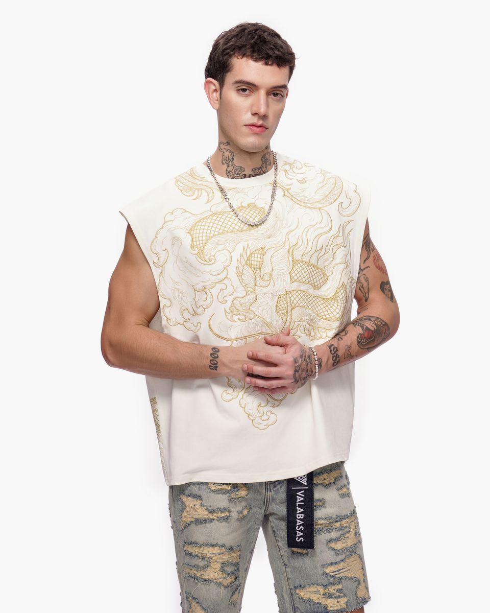 Man wearing a white sleeveless top with gold patterns and camouflage pants on a white background