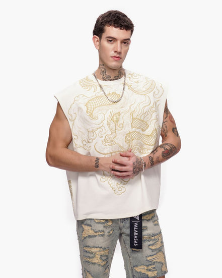 Man wearing a white sleeveless top with gold patterns and camouflage pants on a white background
