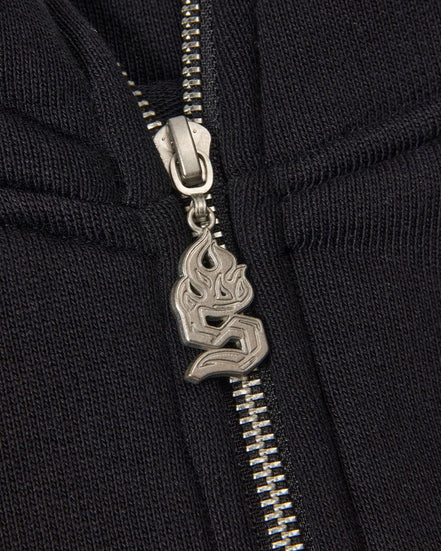 Close-up of a black zipper with a silver flame pendant on a black background