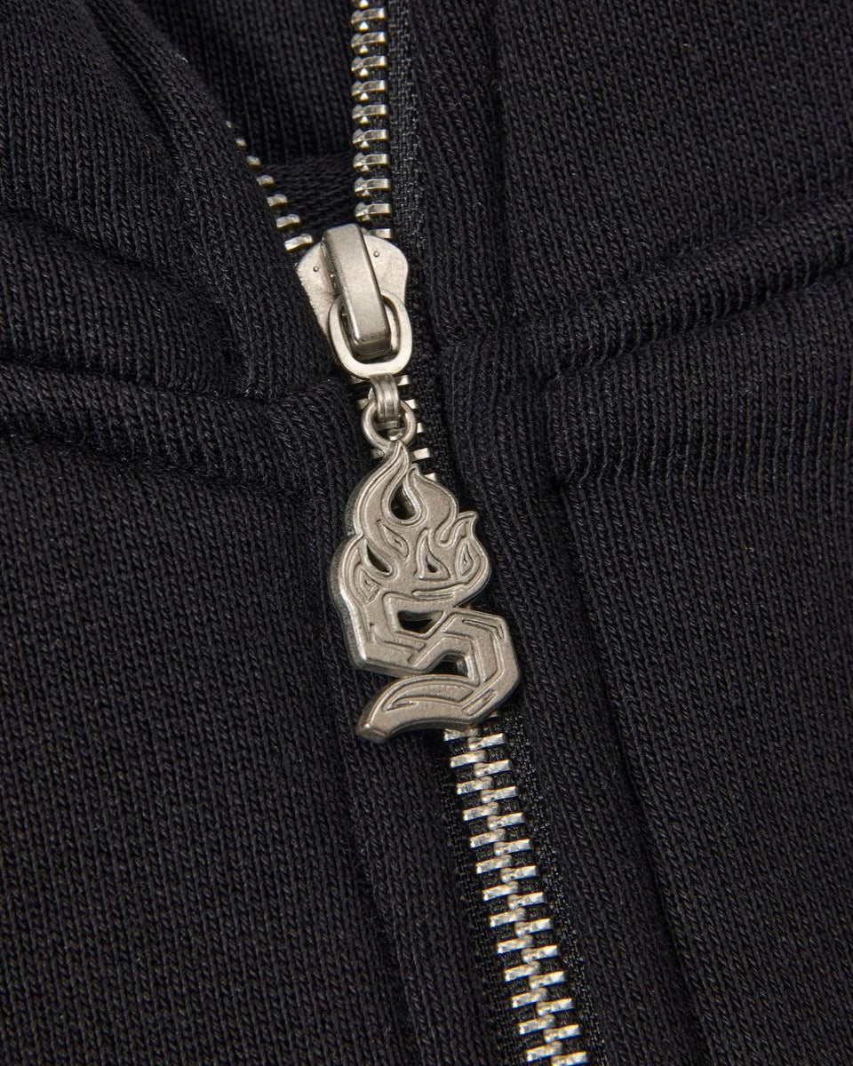 Close-up of a black zipper with a silver flame pendant on a black background
