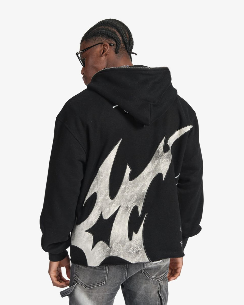 Person wearing a black hoodie with flame design on the back against a white background