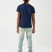 A child model shown from the back wearing a navy blue short-sleeve t-shirt, light-wash distressed jeans, and blue and red sneakers, set against a plain white studio background.