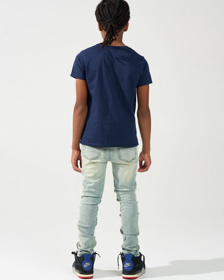A child model shown from the back wearing a navy blue short-sleeve t-shirt, light-wash distressed jeans, and blue and red sneakers, set against a plain white studio background.