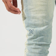 Close-up of a person's hand and thigh wearing light-wash blue denim jeans with a small embroidered logo on the upper leg.