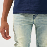 Close-up of a person wearing light-wash blue denim jeans and a navy blue t-shirt against a plain white background.