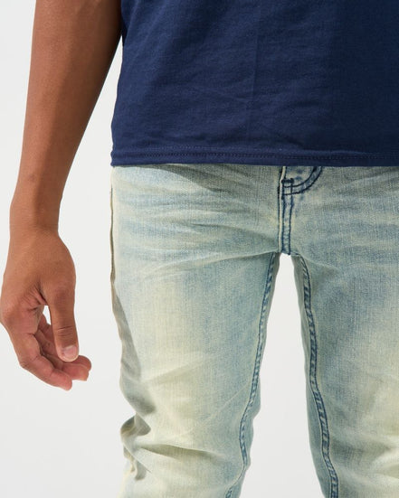 Close-up of a person wearing light-wash blue denim jeans and a navy blue t-shirt against a plain white background.