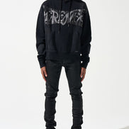 Person wearing a black hoodie with text, black pants, and black shoes with yellow accents on a white background