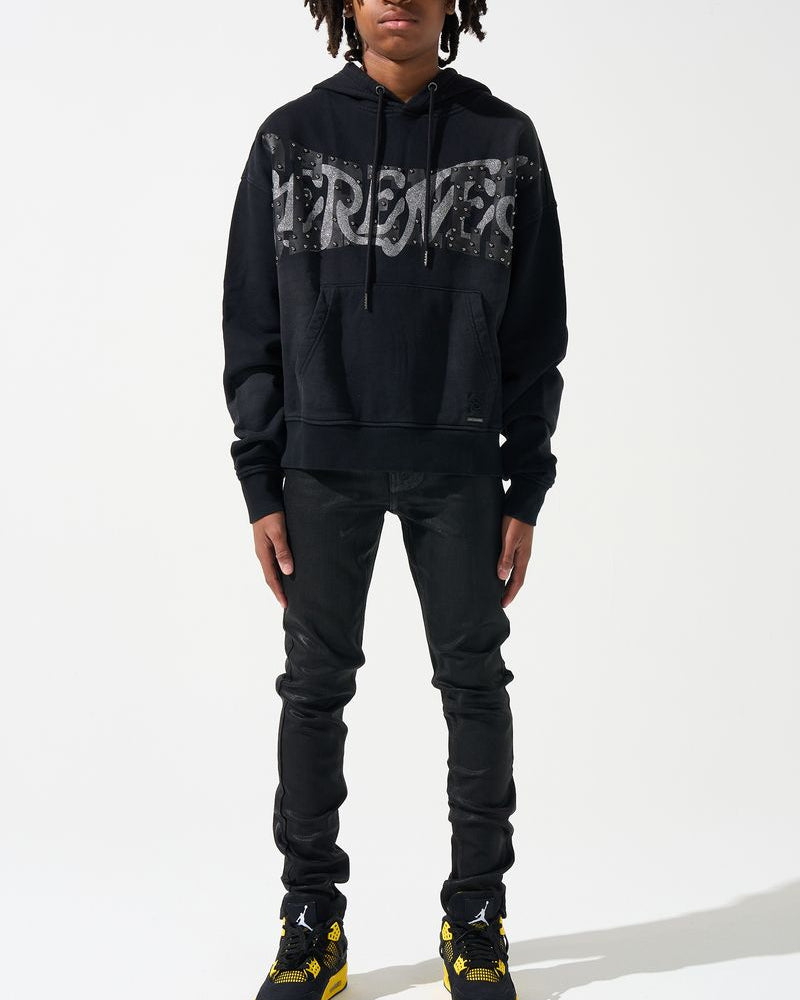 Person wearing a black hoodie with text, black pants, and black shoes with yellow accents on a white background