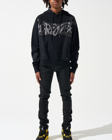 Person wearing a black hoodie with text, black pants, and black shoes with yellow accents on a white background