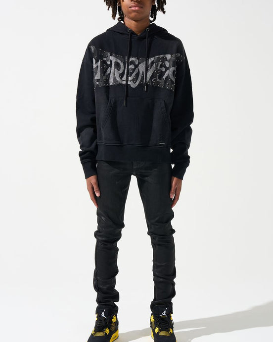 Person wearing a black hoodie with text, black pants, and black shoes with yellow accents on a white background