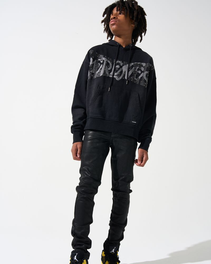Person wearing a black hoodie with graphic design, black leather pants, and black shoes with yellow accents on a white background.
