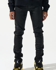 Person wearing black jeans and black sneakers with yellow accents on a white background