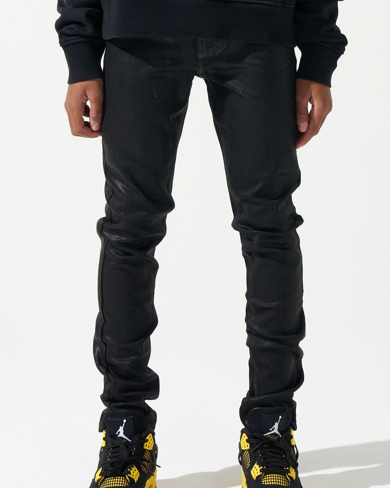 Person wearing black jeans and black sneakers with yellow accents on a white background