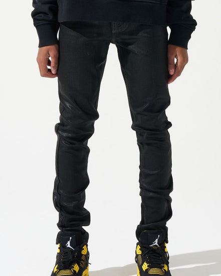 Person wearing black jeans and black sneakers with yellow accents on a white background
