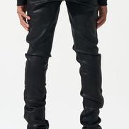 Person wearing black leather pants and black sneakers with yellow accents on a white background