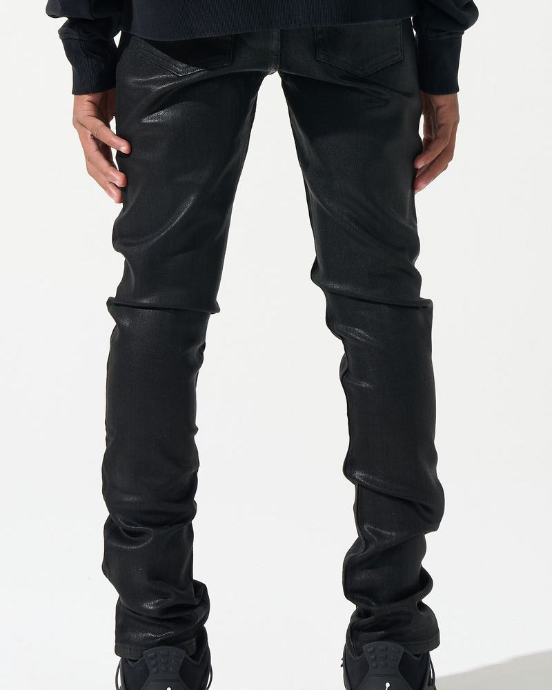 Person wearing black leather pants and black sneakers with yellow accents on a white background
