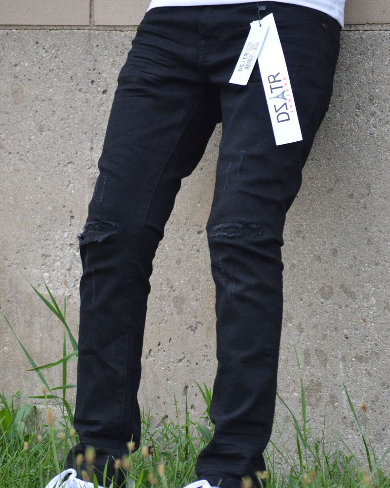 Person wearing black pants with a visible brand tag, standing on grass against a concrete wall.