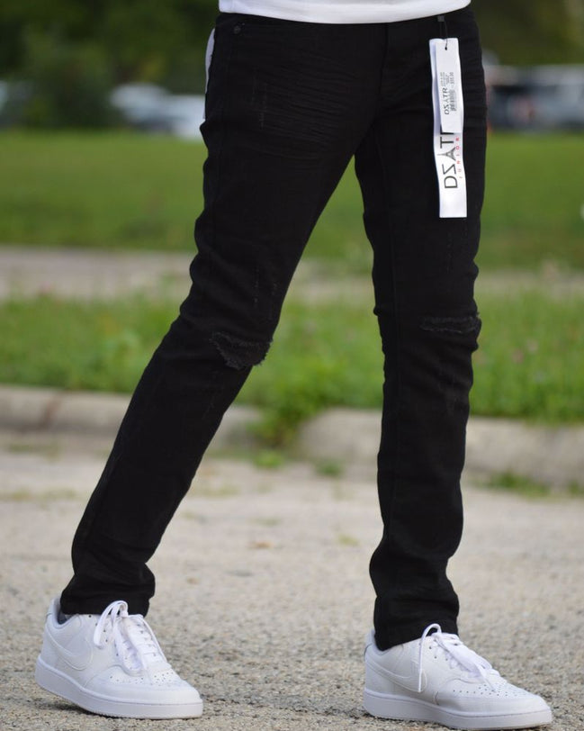 Person wearing black pants with a visible brand logo and white sneakers on a blurred outdoor background