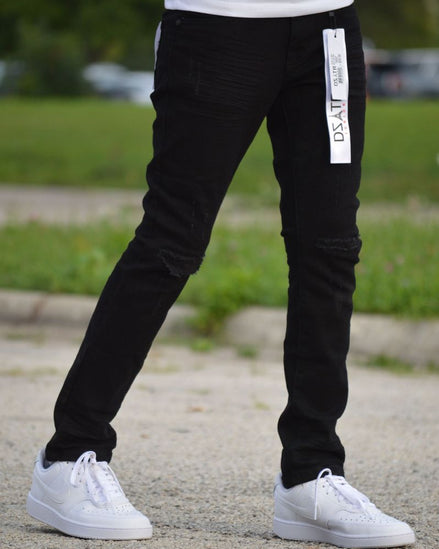 Person wearing black pants with a visible brand logo and white sneakers on a blurred outdoor background