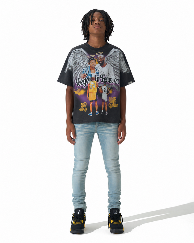 A model wearing a black Los Angeles Lakers graphic t-shirt with a detailed print of Kobe Bryant and Angel, paired with light wash blue jeans and black sneakers, shot against a white studio background.