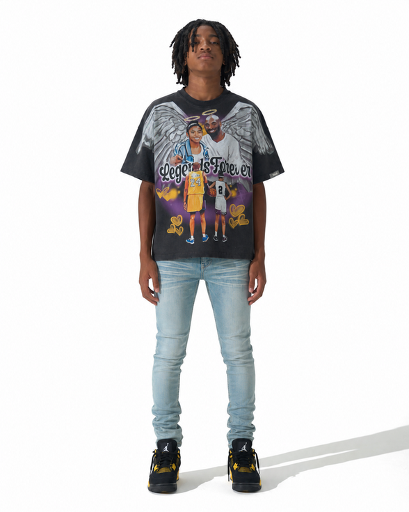 A model wearing a black Los Angeles Lakers graphic t-shirt with a detailed print of Kobe Bryant and Angel, paired with light wash blue jeans and black sneakers, shot against a white studio background.