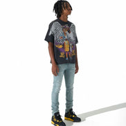 A person standing against a white studio background wearing a black graphic t-shirt, light blue jeans, and black sneakers with yellow accents.