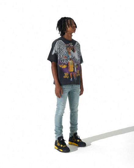 A person standing against a white studio background wearing a black graphic t-shirt, light blue jeans, and black sneakers with yellow accents.