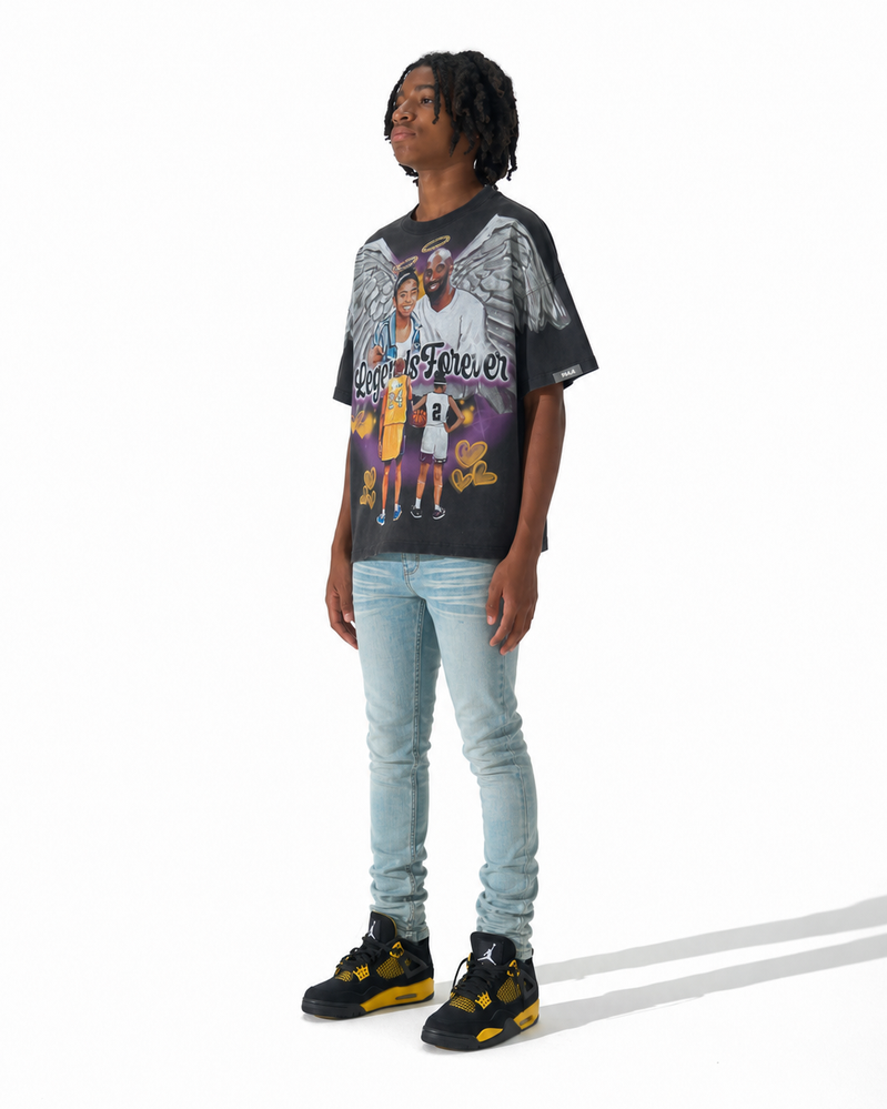A person modeling a black graphic t-shirt with a Los Angeles Lakers print, paired with light-wash blue jeans and black and yellow sneakers, standing against a white studio background.