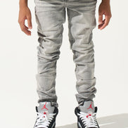 Person wearing light gray jeans and black sneakers with red accents on a white background